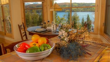 Une table à manger ornée d’un saladier de fruits et d’un arrangement floral, le tout mis en valeur par une vue pittoresque sur un lac.