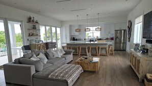 Ein großzügiger Wohnbereich mit grauem Sofa, Couchtisch aus Holz und einer Küche mit weißen Schränken und einer großen Kochinsel.