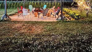 Un espace extérieur aménagé avec des chaises et des tables, des guirlandes lumineuses suspendues et un jardin en arrière-plan.