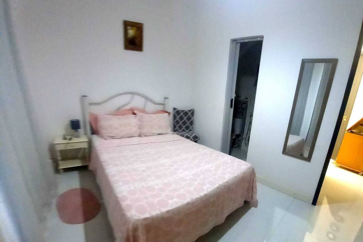 A bedroom with a bed, a nightstand, a bedside table, a mirror, and a door.