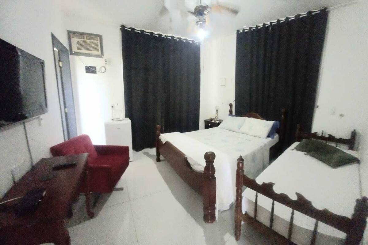 A bedroom with two single beds, a desk, a chair, a TV, and a ceiling fan.