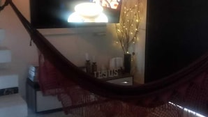 Uma sala de estar com televisão na parede, uma rede e uma escada.