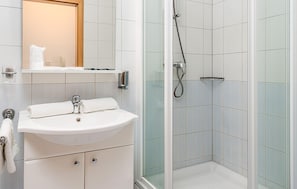 Ein Badezimmer mit einem weißen Waschbecken, einem Spiegel und einer Duschkabine mit gefliesten Wänden.