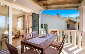 A balcony with a wooden table and chairs, a potted plant, and a view of the sky and buildings. - Amazing apartment in Palit with house sea view (Palit)