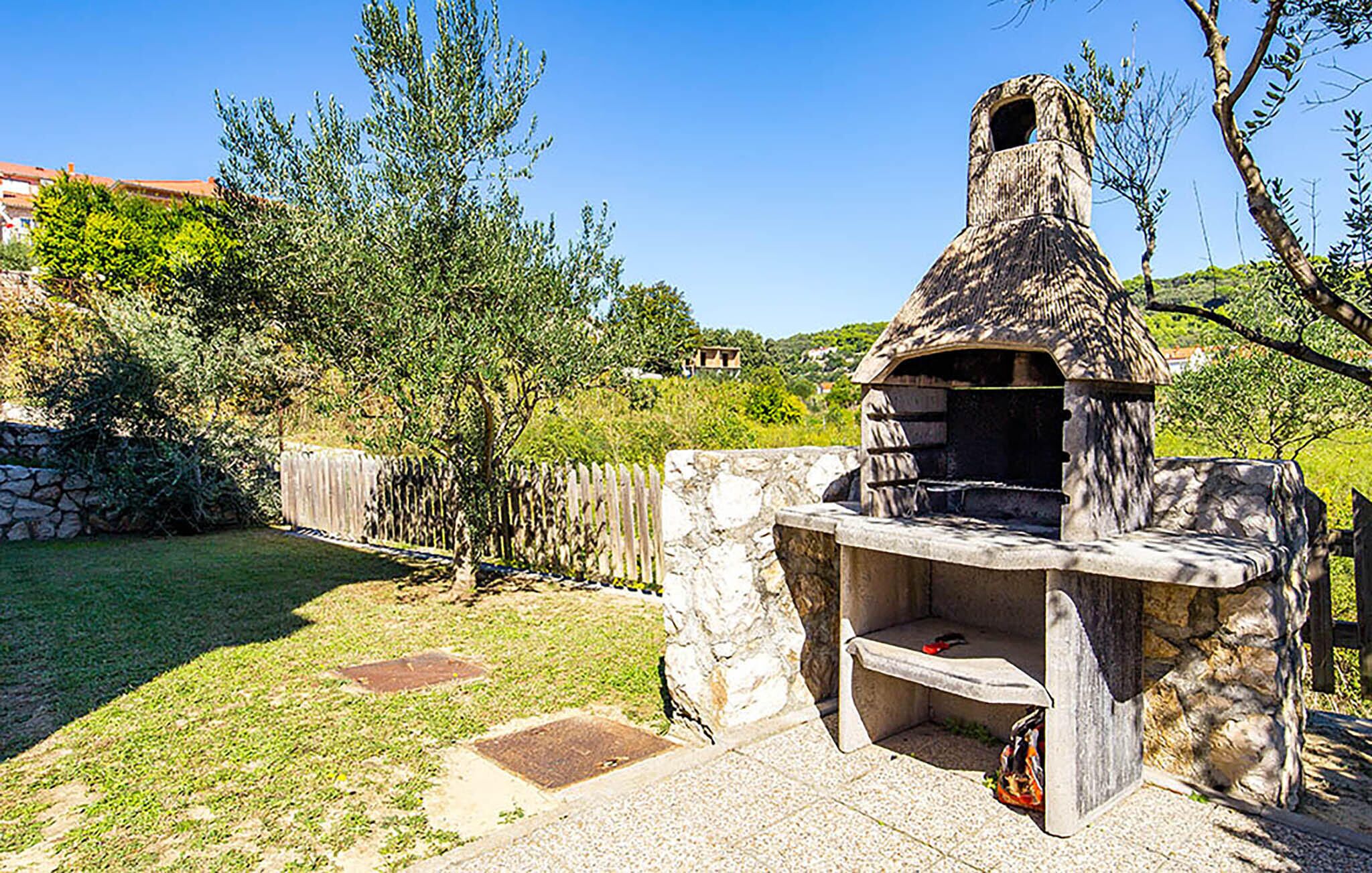Un área de barbacoa de piedra al aire libre con chimenea, rodeada por un muro de piedra y un césped.