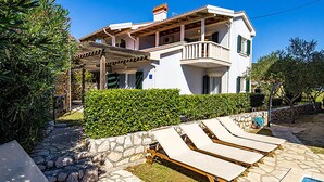 Une maison à deux étages dotée d’un balcon, d’un mur en pierre et d’un espace piscine avec des chaises longues.