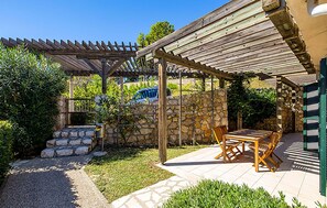 Un patio cubierto con muro de piedra, pérgola y una mesa con sillas.