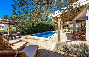 Un área de piscina con sillones, una pérgola y un patio cubierto con mesas y sillas.