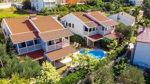Um edifício residencial com vários andares, com piscina, cercado por vegetação e outras construções residenciais.