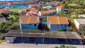 Zona residencial costeira com casas de telhado vermelho, área de estacionamento e um porto de recreio ao fundo.