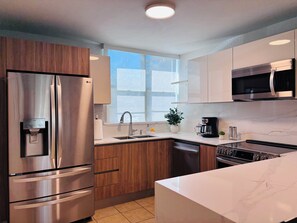A modern kitchen with stainless steel appliances, wooden cabinets, a marble countertop, and a window providing natural light. - Famous beach resort, 5 pools & children's water park / full air conditioning / ocean view (Loiza)