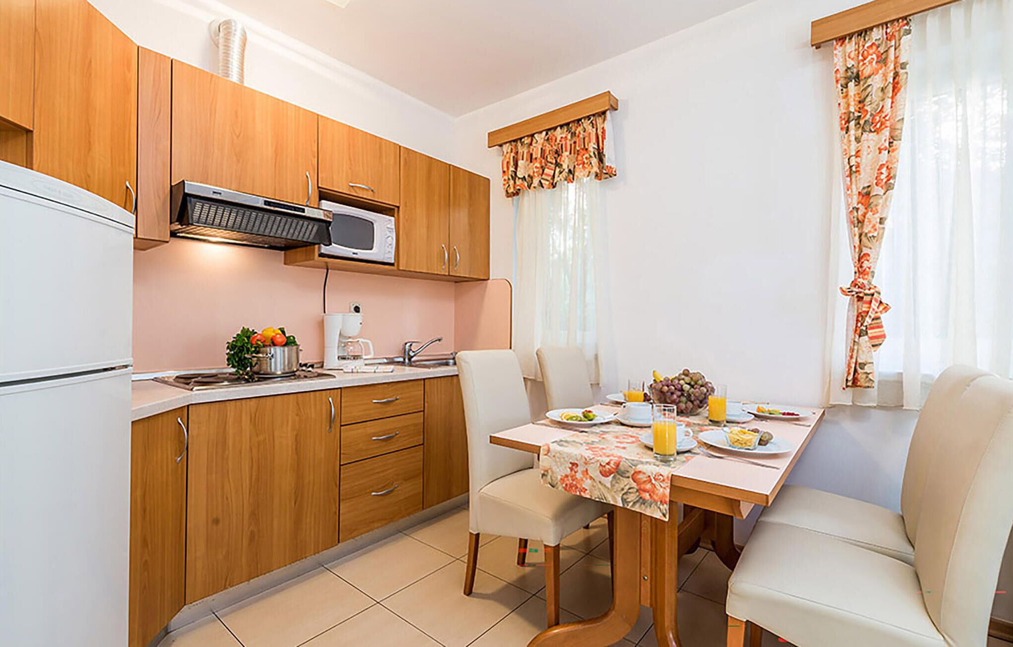 Une cuisine compacte avec des meubles en bois, un four à micro-ondes et une machine à café. On y trouve une table à manger avec des chaises et une table préparée pour le petit-déjeuner.