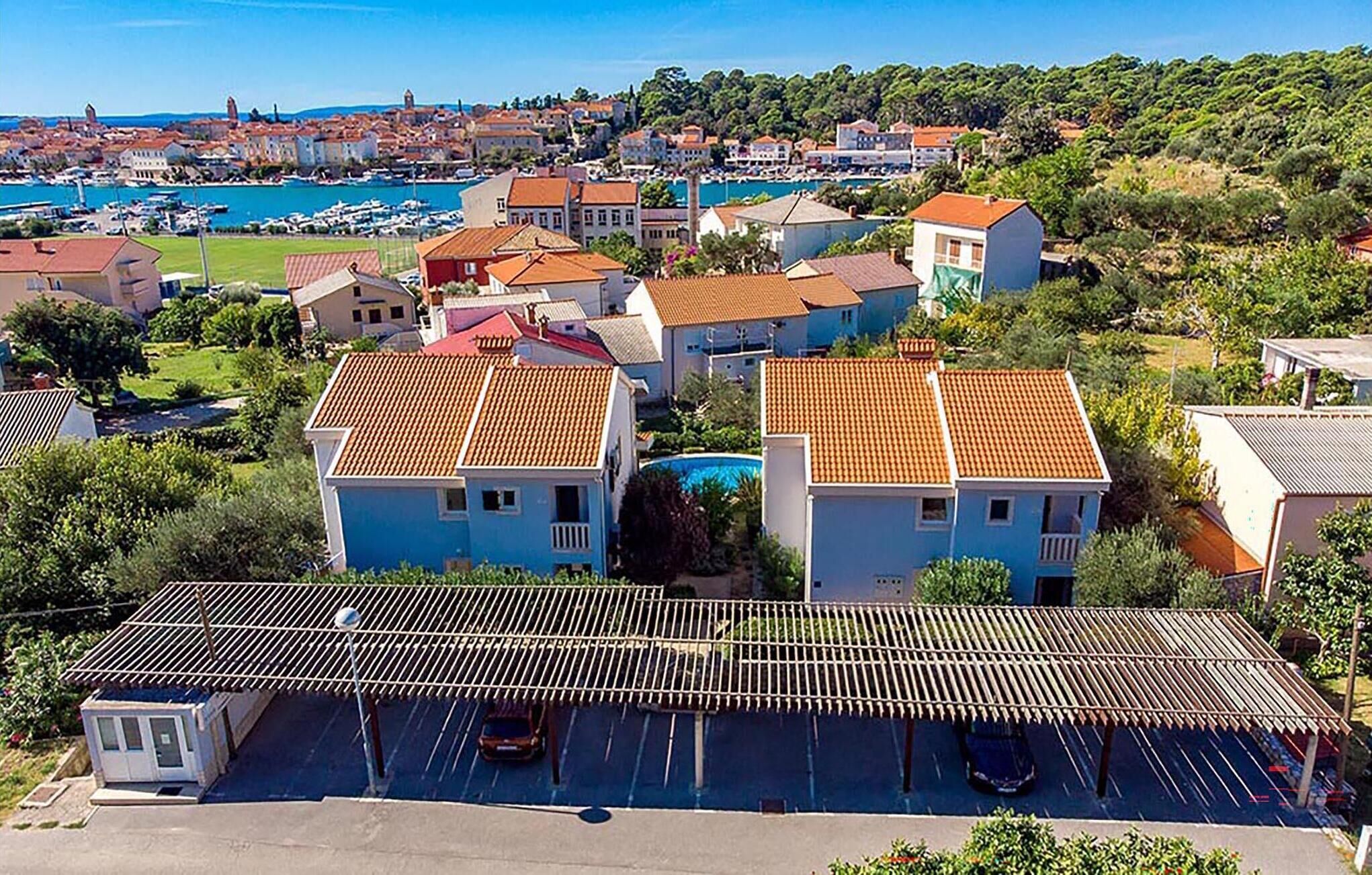 Un quartier résidentiel situé sur la côte, avec des maisons dotées de toits recouverts de tuiles rouges et un espace de stationnement comprenant un abri-voiture couvert.