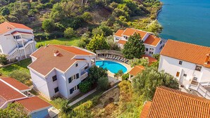 A coastal residential area with houses featuring red-tiled roofs, a central swimming pool, and a view of the sea. - Gorgeous apartment in Kampor with WiFi (Kampor)