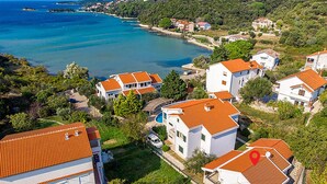 Vista aérea de uma área residencial costeira com casas de telhado vermelho, cercada por vegetação e um mar azul cristalino.