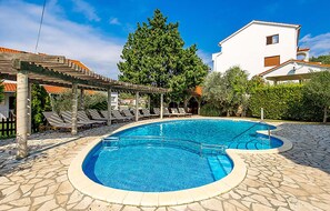 A swimming pool with lounge chairs and a pergola, surrounded by stone tiles and greenery. - Stunning home in Kampor (Kampor)