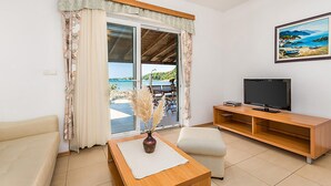 A living room with a sofa, a coffee table, a TV, and a view of the sea through a sliding glass door. - Nice apartment in Kampor (Kampor)