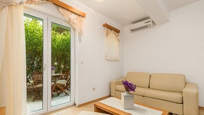 A living room with a beige sofa, a wooden coffee table, and a sliding glass door leading to an outdoor area with a table and chairs. - 1 bedroom beach front apartment in Kampor (Kampor)