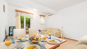 A dining area with a table set for breakfast, including plates of food, drinks, and a bowl of fruit. There is a sofa and a TV in the background. - 1 bedroom beach front apartment in Kampor (Kampor)