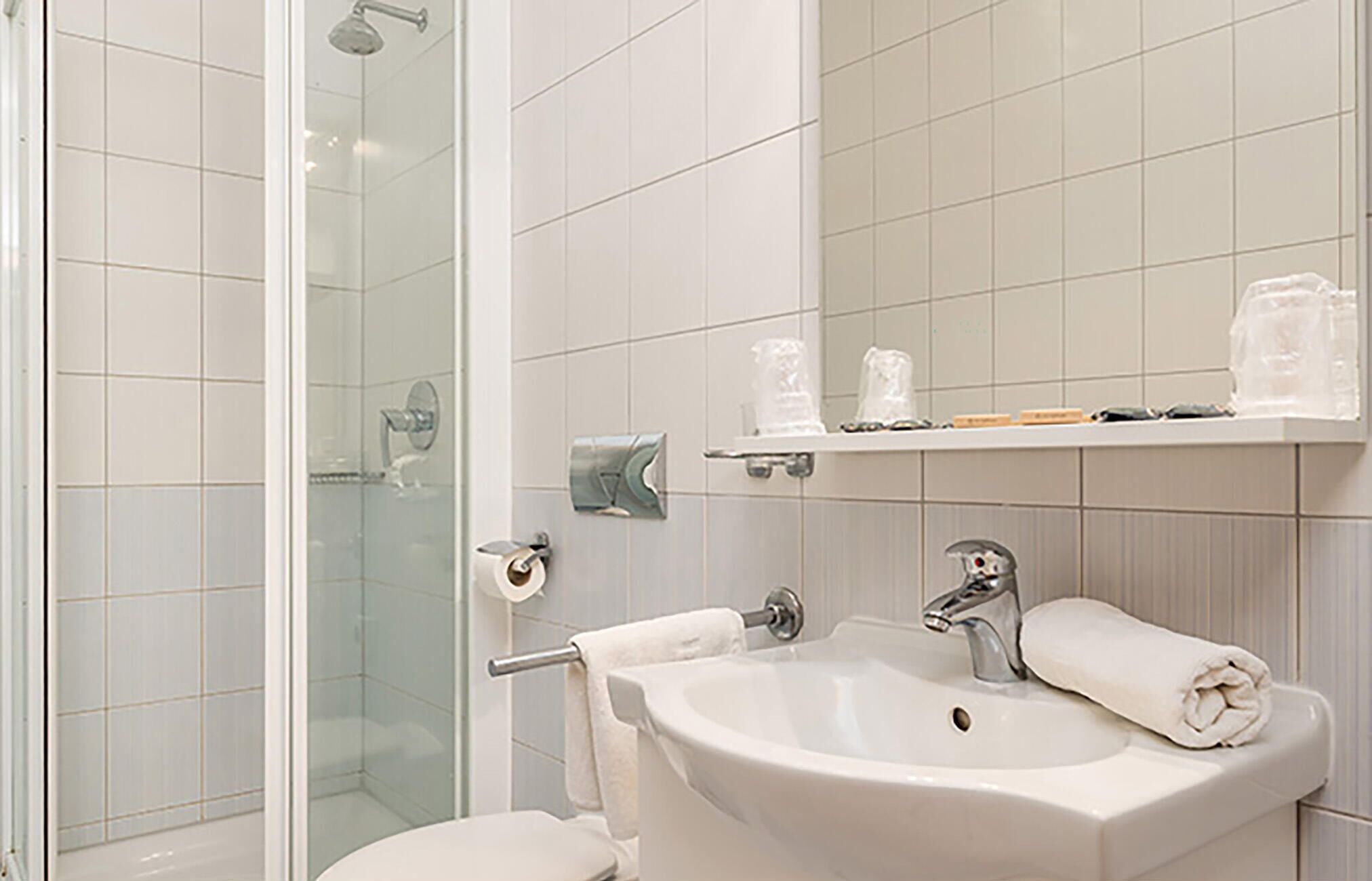 A bathroom with a glass shower enclosure, a sink with a towel, and a mirror above the sink.