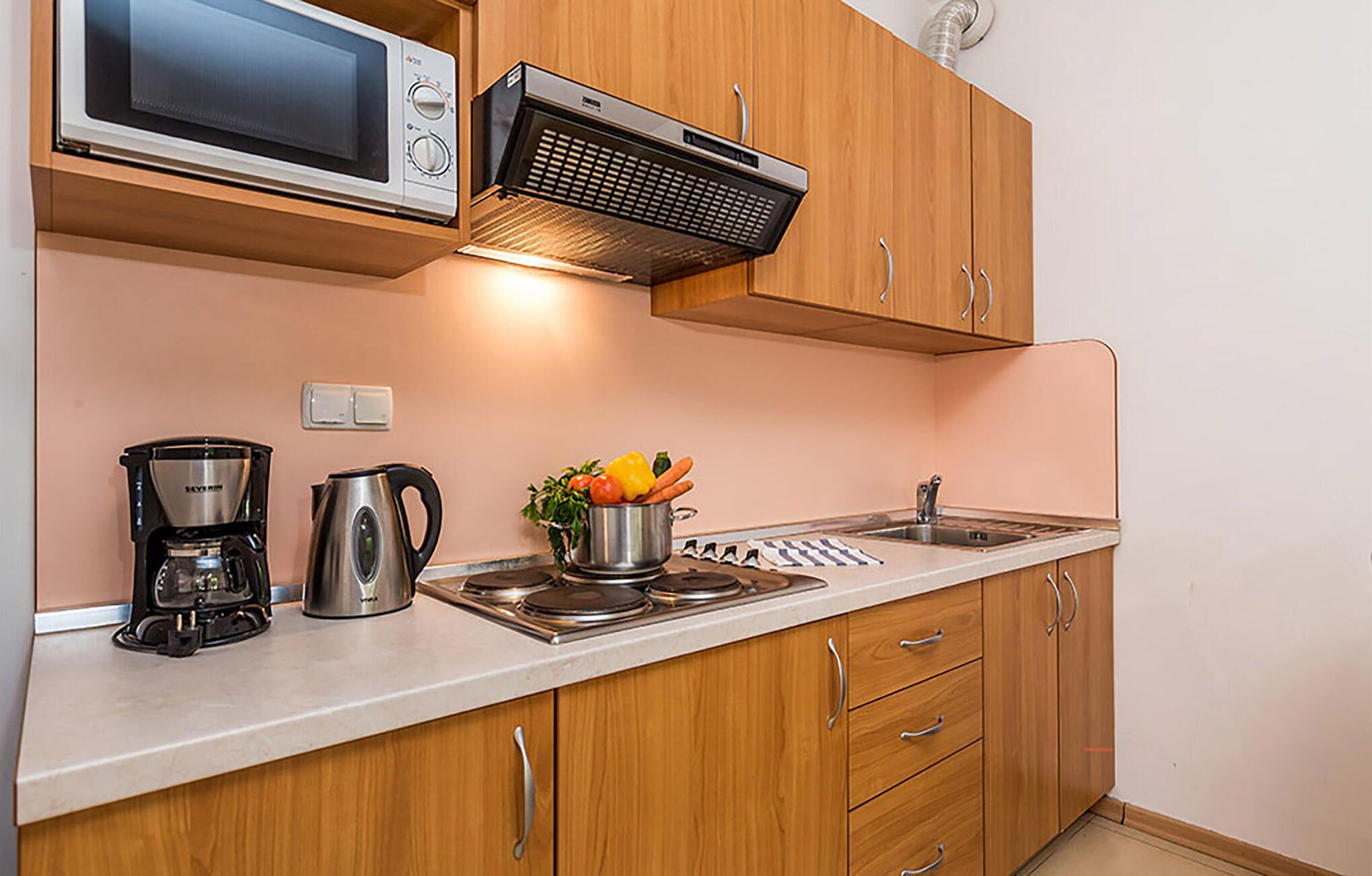 A kitchen with wooden cabinets, a microwave, a stove, a coffee maker, and a kettle.
