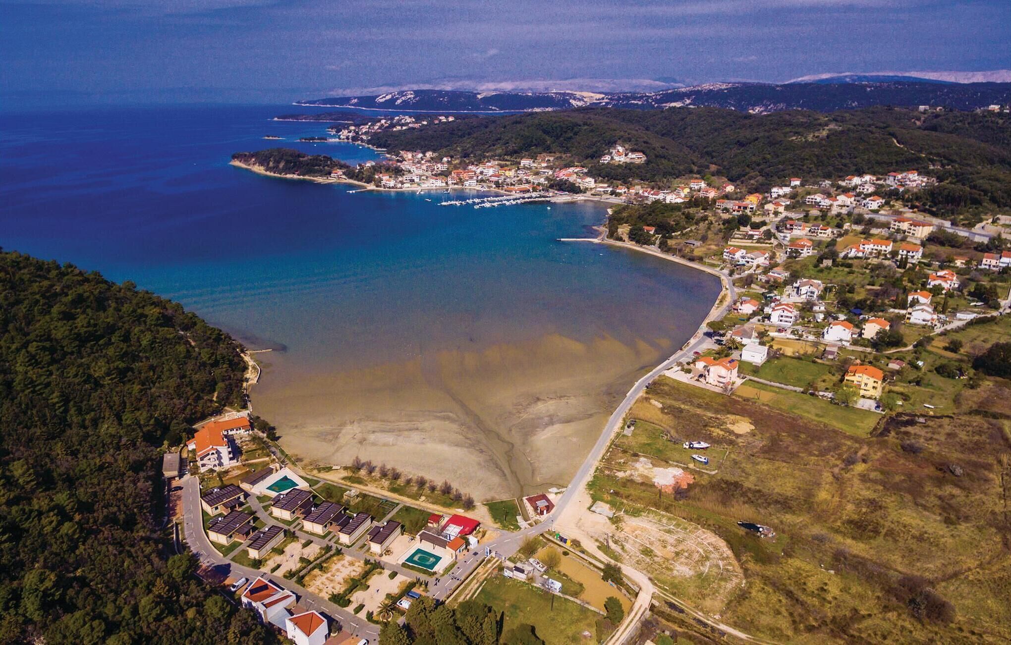 An aerial view of a coastal town with a marina, residential areas, and a beach.