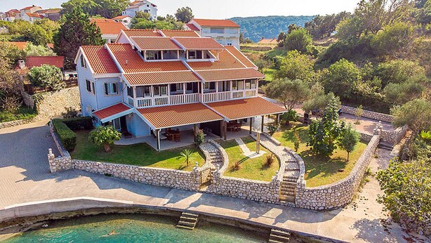 Ein zweistöckiges Haus mit Swimmingpool, umgeben von Steinmauern und viel Grün.
