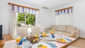 Ein modernes Wohnzimmer mit einer Couch, einem Esstisch mit Frühstück gedeckt und großen Fenstern mit Vorhängen.