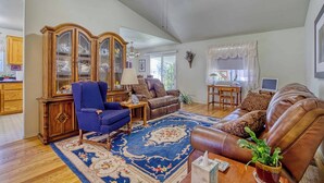 Un salon spacieux comprenant un grand meuble en bois, un fauteuil bleu, un canapé en cuir marron et un tapis bleu à motifs.