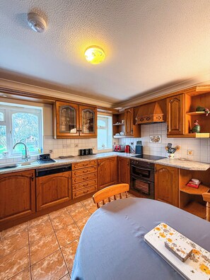 Une cuisine avec des meubles de rangement en bois, un évier, une cuisinière et une table à manger recouverte d’une nappe à motifs floraux.
