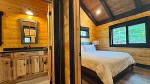 Interior de una cabaña de madera con cama, baño y zona de cocina.