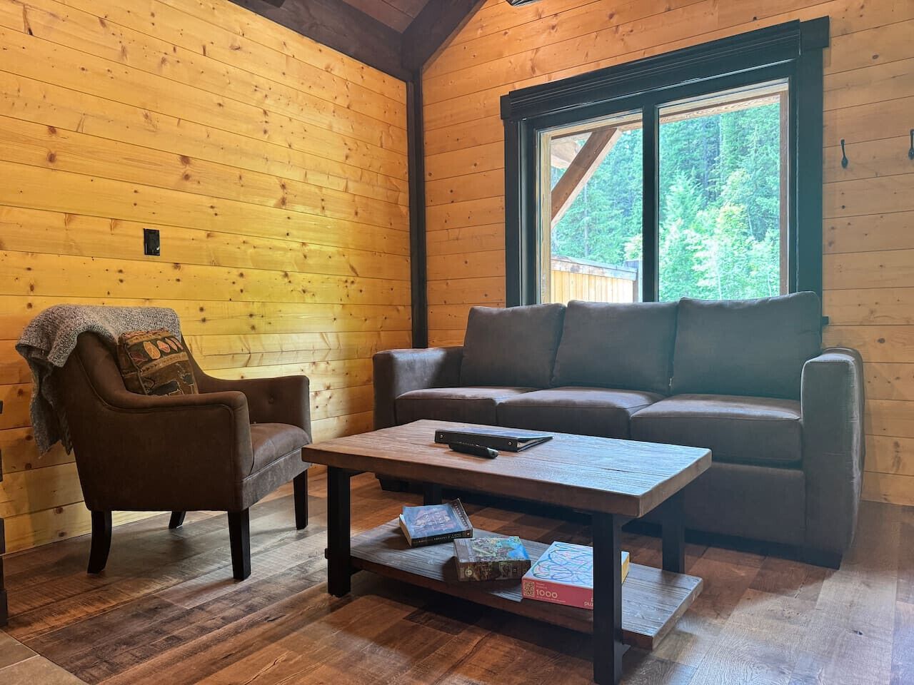 A cozy cabin interior with a wooden wall, a sofa, a chair, and a coffee table.