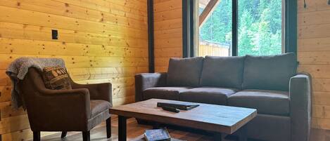 A cozy cabin interior with a wooden wall, a sofa, a chair, and a coffee table.