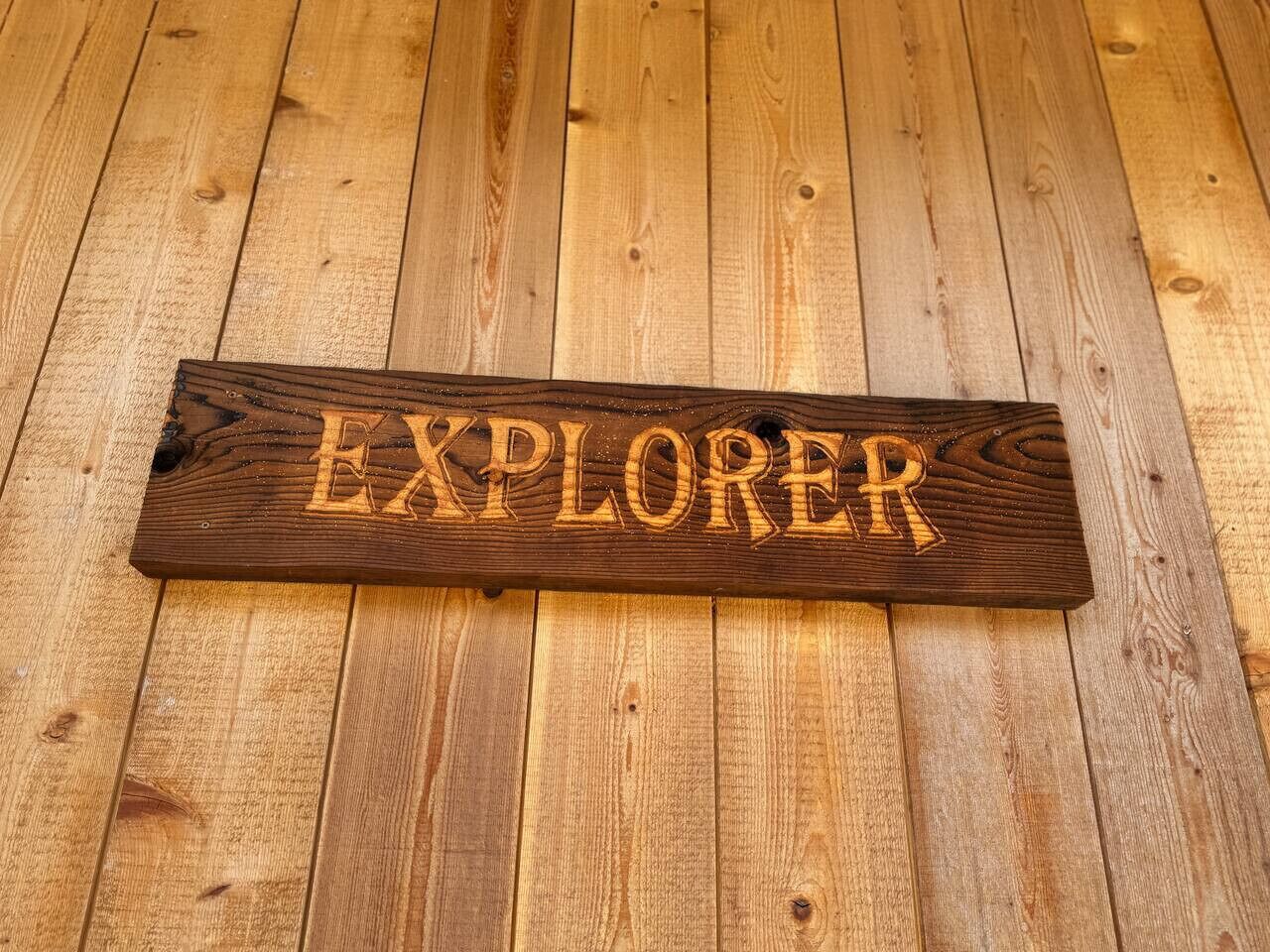 A wooden sign with the word "EXPLORER" carved into it, placed on a wooden floor.