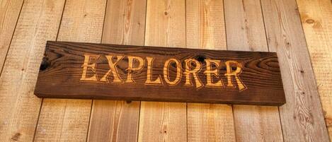 A wooden sign with the word "EXPLORER" carved into it, placed on a wooden floor.