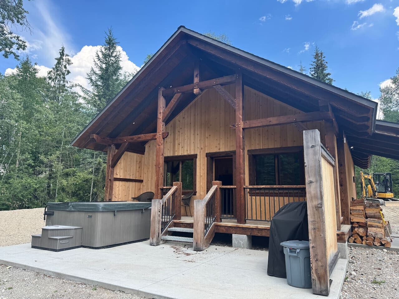 A wooden cabin with a covered porch, a hot tub, and a grill area.