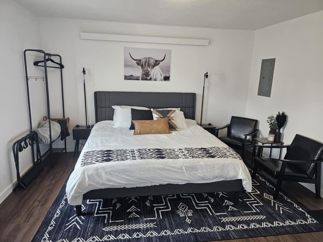 Un dormitorio moderno con una cama grande, cabecera, mesita de noche, una silla, una lámpara colgante y un cuadro en la pared.