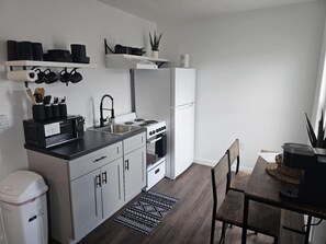 Une cuisine de taille réduite avec des meubles blancs, un plan de travail noir, une cuisinière et un réfrigérateur.