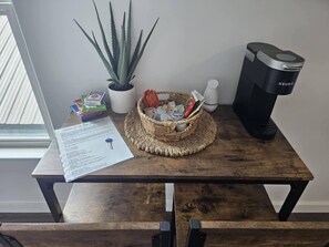 Une table en bois sur laquelle se trouvent un panier de livres, une plante en pot et une machine à café Keurig.