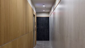 A narrow hallway with wooden paneling on one side and tiled walls on the other, leading to a dark door at the end. - Hoboken Loft Hideaway - Walk to Path (Hoboken)