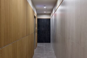 A narrow hallway with wooden paneling on one side and tiled walls on the other, leading to a dark door at the end. - Hoboken Loft Hideaway - Walk to Path (Hoboken)