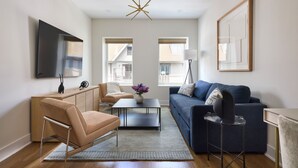 A modern living room with a sofa, armchair, coffee table, and a TV mounted on the wall. - Hoboken Loft Hideaway - Walk to Path (Hoboken)