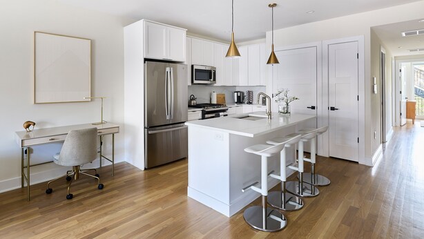 A modern kitchen with white cabinetry, stainless steel appliances, and a central island with bar stools. - Hoboken Loft Hideaway - Walk to Path (Hoboken)