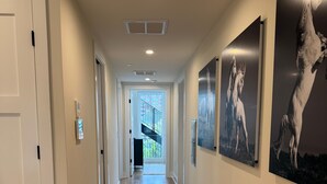 Un pasillo con suelo de madera, paredes blancas y una puerta a la izquierda. Se observan tres pinturas blanco y negro de caballos en la pared derecha.