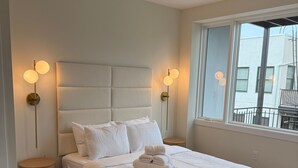 Un dormitorio con cama, una mesita de noche de madera redonda, un ventilador de techo y dos lámparas fijadas a la pared.