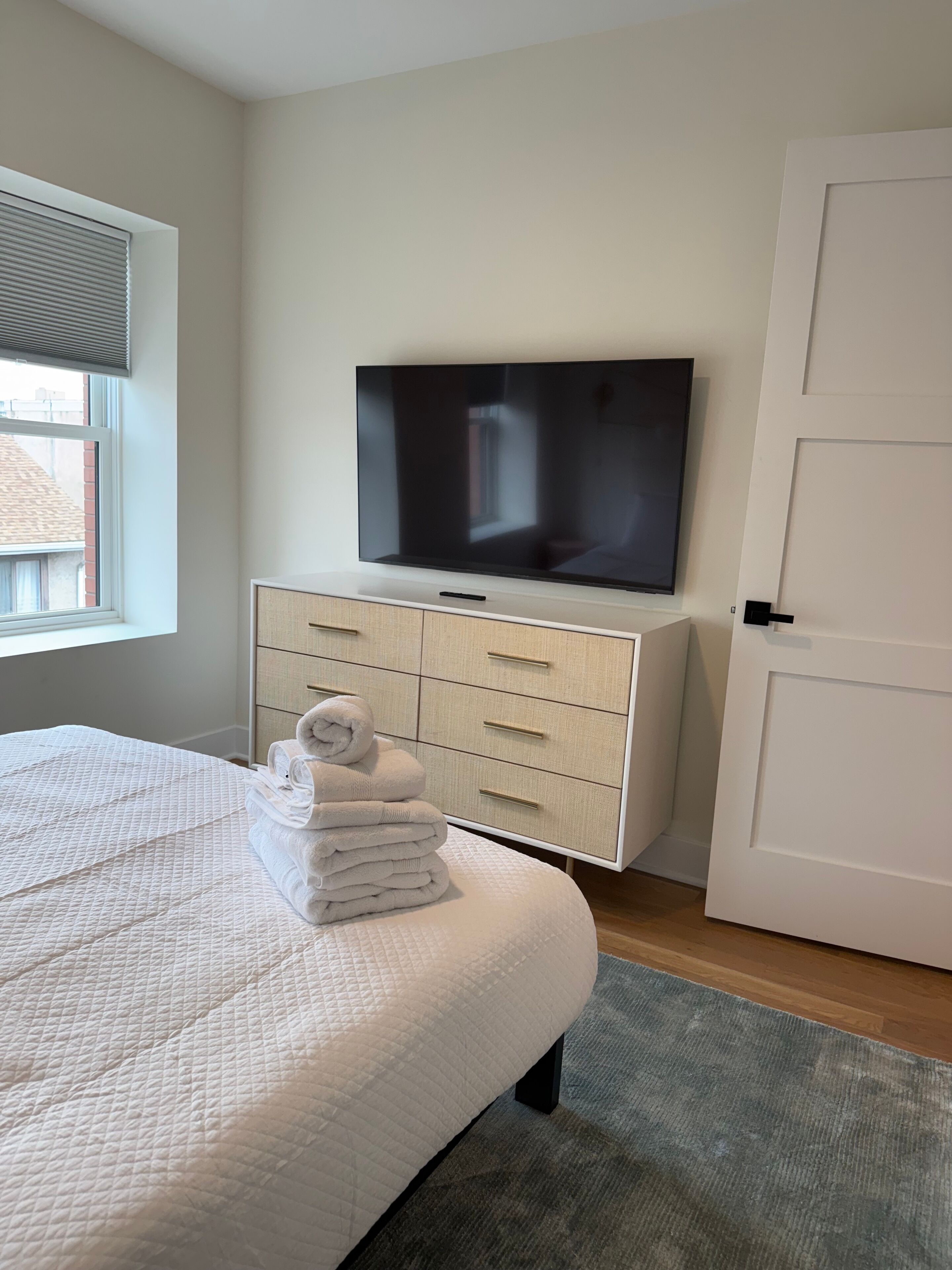 A bedroom with a bed, a TV, a dresser, and a door.