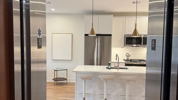Una cocina moderna con electrodomésticos de acero inoxidable, una isla central con taburetes de bar e iluminación colgante.