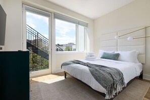 A modern bedroom with a large bed, a view of a cityscape through a window, and a staircase leading to an outdoor area. - Bright 3BR Loft Hoboken Gem (Hoboken)