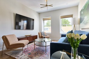 A modern living room with a sofa, armchair, coffee table, and a TV mounted on the wall. - Bright 3BR Loft Hoboken Gem (Hoboken)