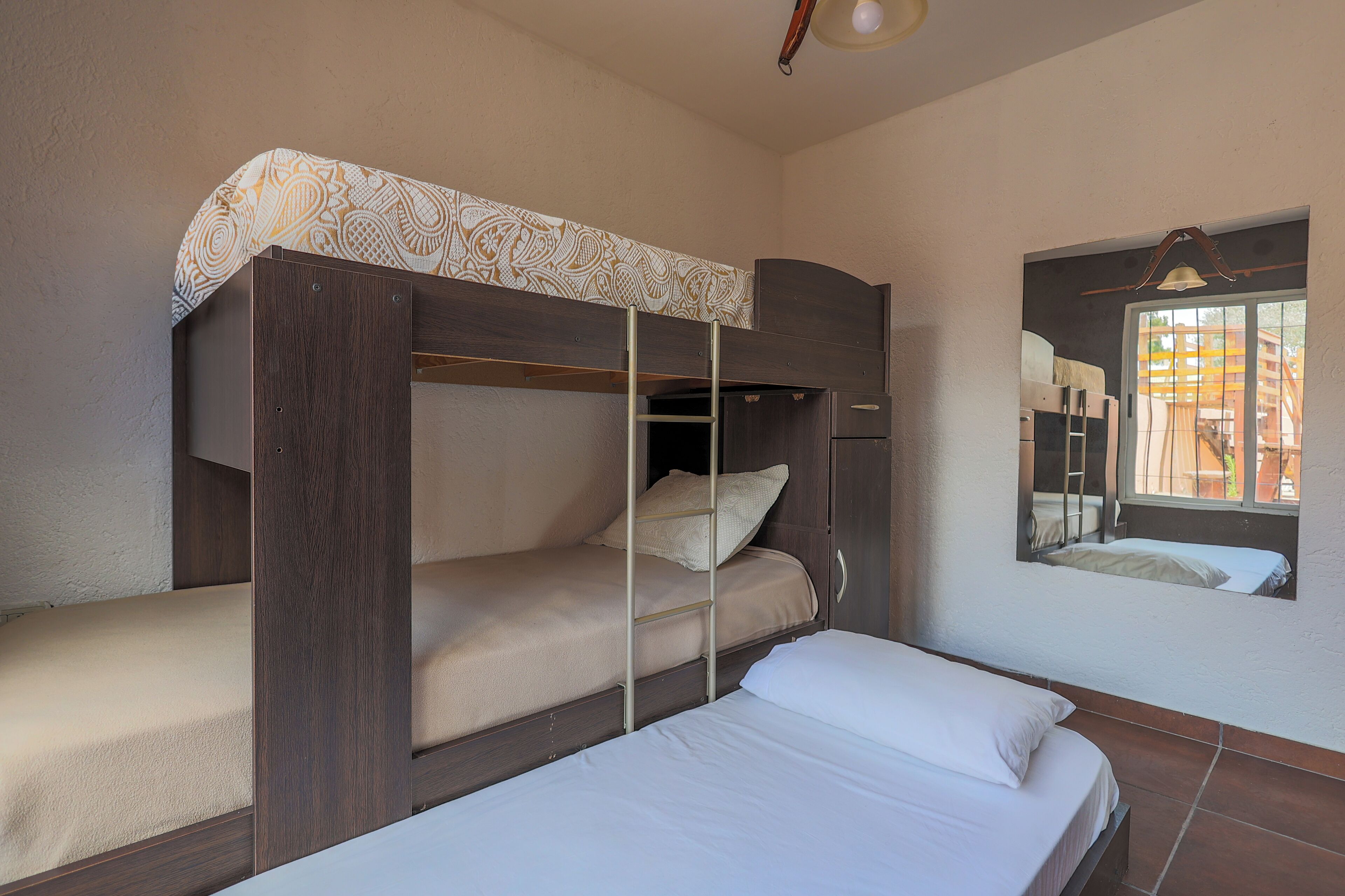 A bunk bed with a ladder, a single bed, and a window with a view of buildings.